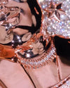Close-up of a highly reflective rose gold metallic surface with a rhinestone necklace and sparkling star-shaped embellishments.