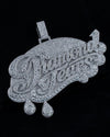 A large silver-tone nameplate pendant covered in clear rhinestones, featuring the words 'Diamond Jaxx' in cursive with two dangling teardrop charms, shown on a black background.