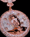 A close-up of a large oval pendant covered in sparkling clear stones, featuring a rose-gold-toned portrait of a man wearing sunglasses, surrounded by moon and star motifs on a black background.