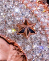 A close-up of a metallic rose gold star-shaped pin or brooch resting on a sparkling, rhinestone-covered surface.