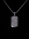 A silver dog tag pendant necklace paved with sparkling clear stones, hanging from a matching silver ball chain against a solid black background.