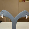 Diamond earrings on a gray stand against a beige wall.