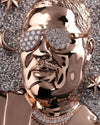 A close-up of a highly polished rose gold figurine or sculpture of a man's face wearing diamond-encrusted sunglasses, set against a glittering silver background with star and moon motifs.